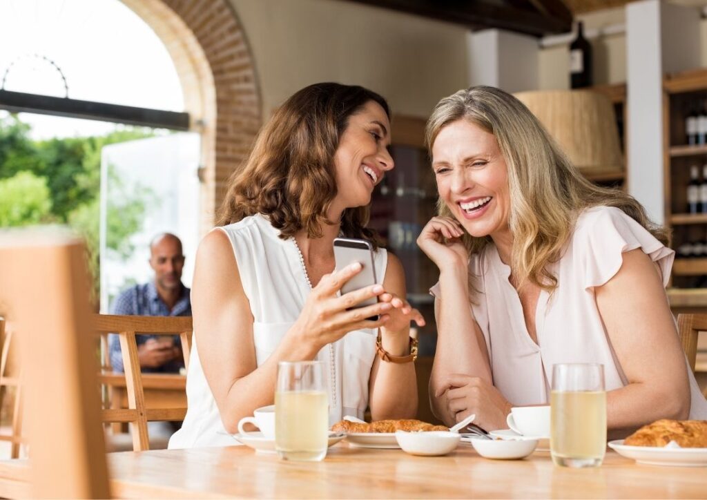 2 vrouwen lachen en kletsen samen onder het genot van een kop koffie