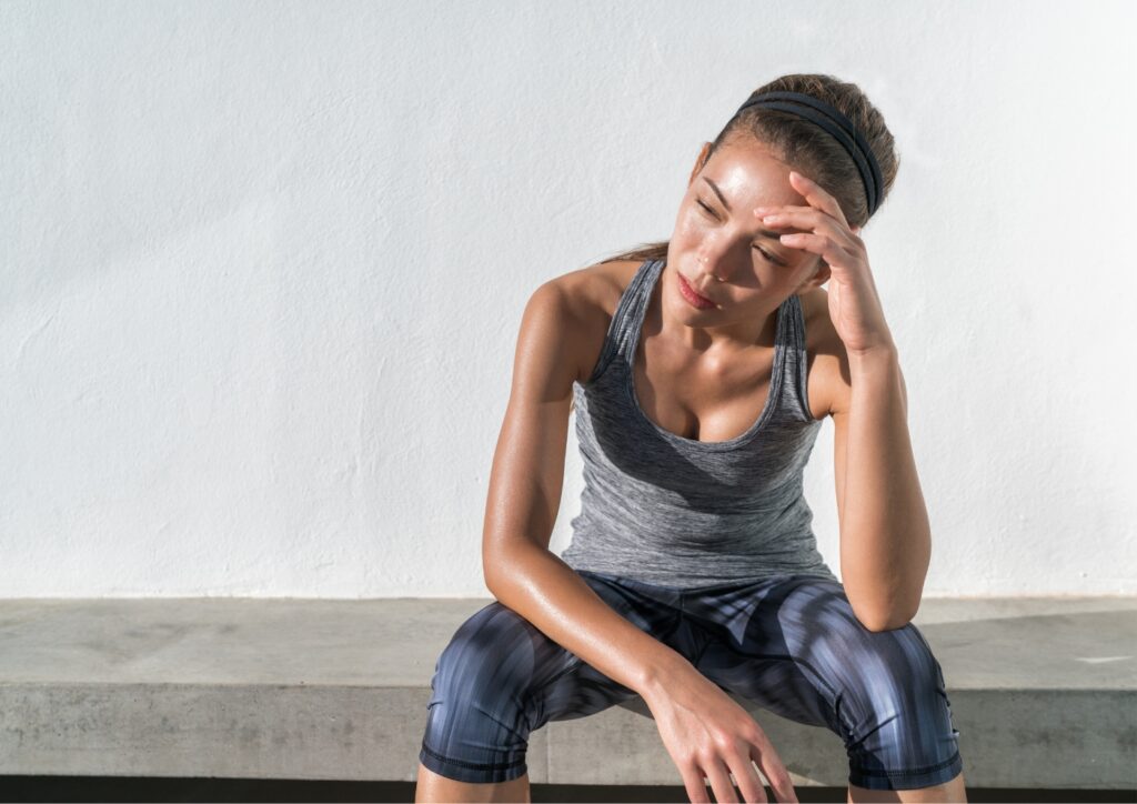 Bezwete vrouw in sportkleding zit vol in de zon, is vermoeid