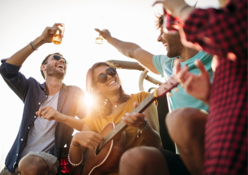 Vrienden hebben plezier. Een vrouw speelt op haar gistaar en vrienden staan om haar heen te lachen en dansen meet een glas in hun hand.