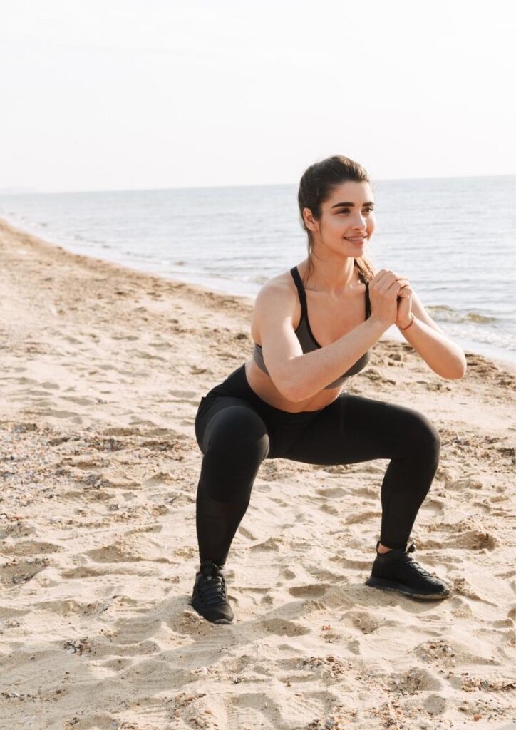 Vrolijke, vitale jonge vrouw doet de oefening de squat op het strand