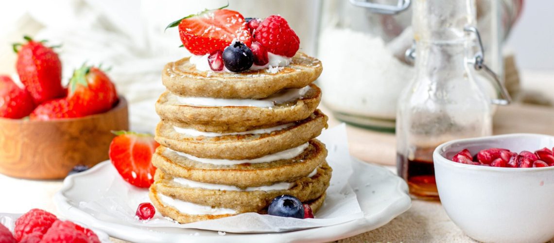 Bord met gestapelde pancakes met laagjes kwark en stukjes fruit als topping