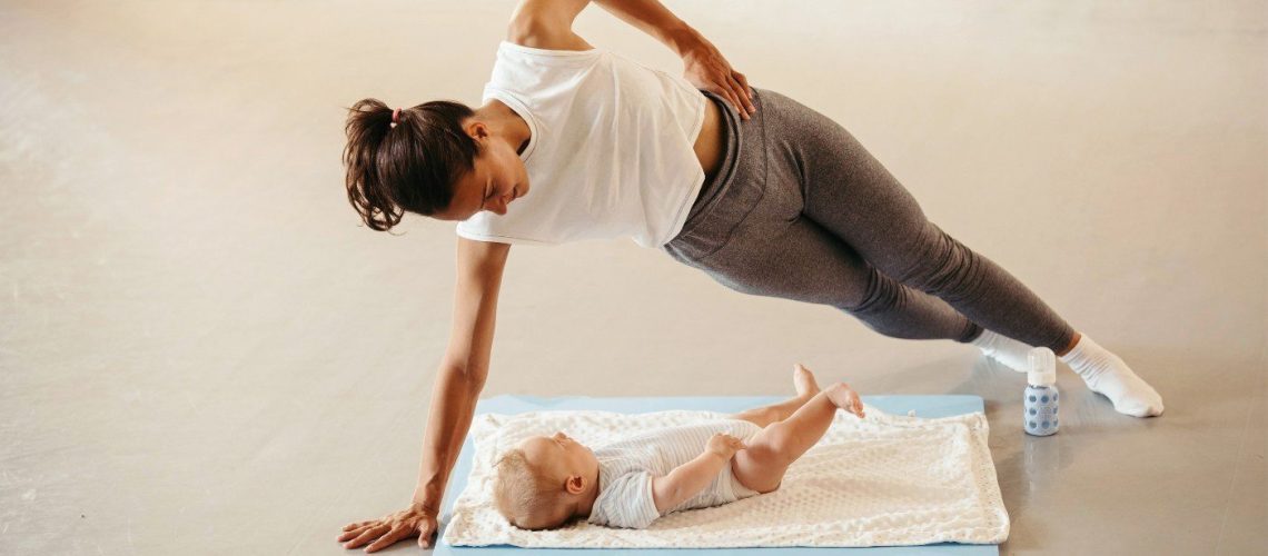 Vrouw in sportkleding traint, terwijl ze lachend kijkt naar haar liggende baby. Vrouw hangt als ware boven de baby, steunend op 1 arm. Andere arm houdt zij in haar zijde.